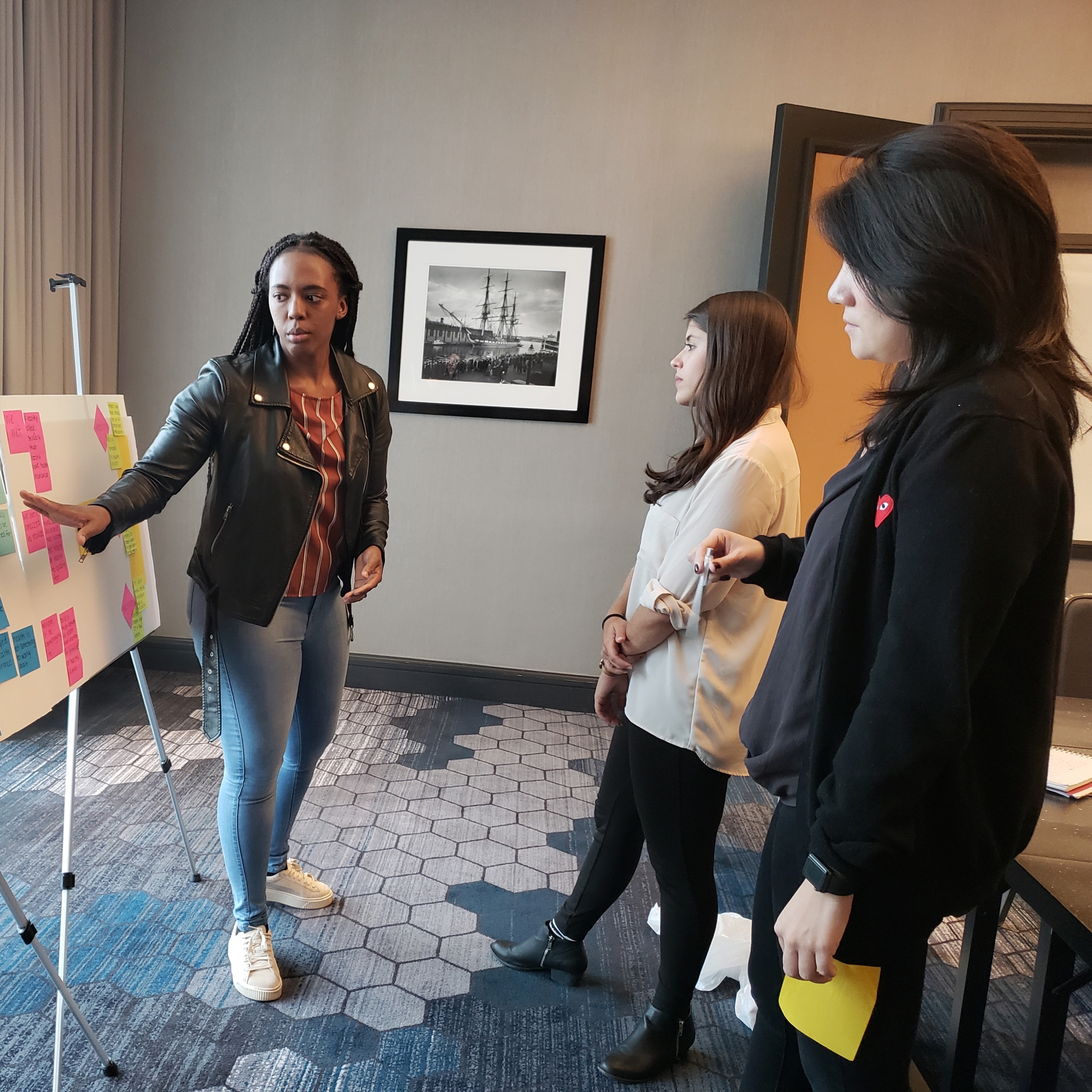 Three students gathered around an idea board with yellow, blue, and pink notes
