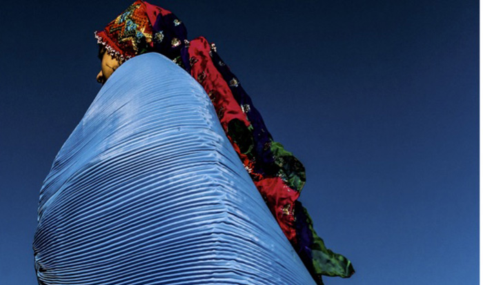 An Afghan woman in elaborate clothing with a blue pleated shawl