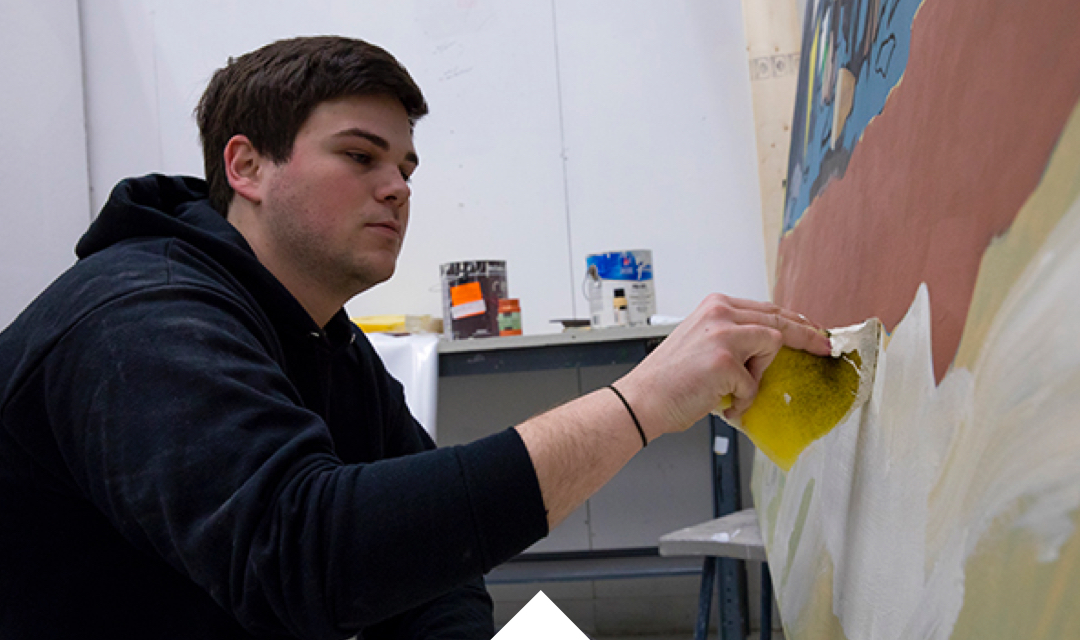 Case Baumgarten sits at a canvas painting a work in progress