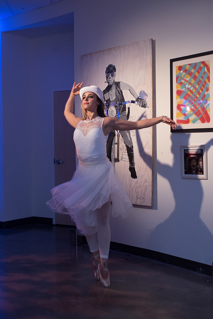 A dancer dressed in white spins in front of a wall covered in visual art.