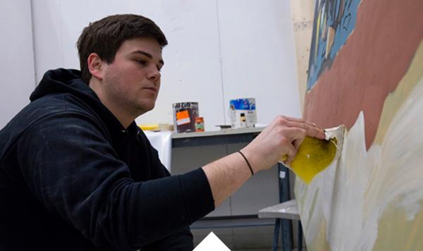 Case Baumgarten sits at a canvas painting a work in progress